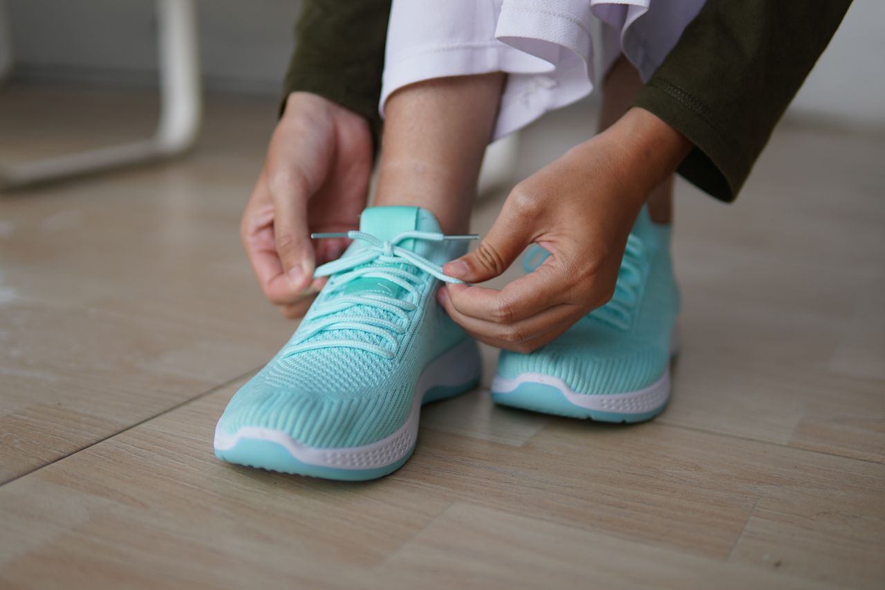 Close-up of hands tying shoelaces on vibrant blue running shoes, emphasizing athletic focus and style.